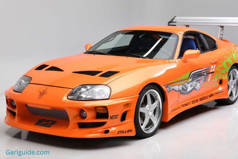 An orange Toyota Supra with a black hood parked, showcasing its sleek design and sporty features.